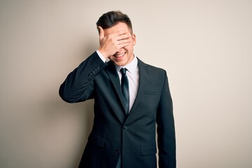 Young handsome business man wearing elegant suit and tie over isolated background smiling and laughing with hand on face covering eyes for surprise. Blind concept.