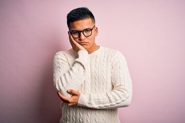 Young handsome latin man wearing white casual sweater and glasses over pink background thinking...