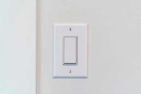 Electrical rocker light switch with flat broad lever on white interior wall