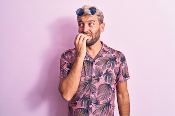 Handsome blond man on vacation wearing casual shirt and sunglasses over pink background looking stressed and nervous with hands on mouth biting nails. Anxiety problem.