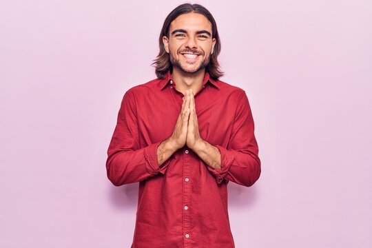 Young handsome man wearing business clothes praying with hands together asking for forgiveness smiling confident.