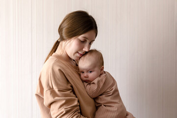Cheerful beautiful young woman holding baby girl in her hands and looking at her with love at home