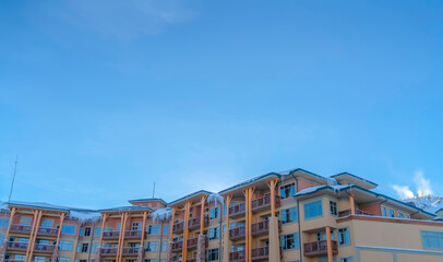Residential building with icicles on the snowy roof against blue sky in winter