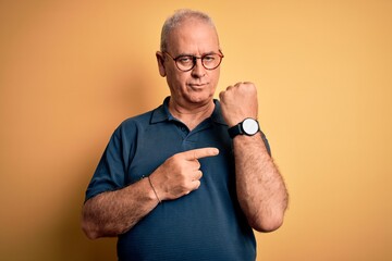 Middle age handsome hoary man wearing casual polo and glasses over yellow background In hurry...