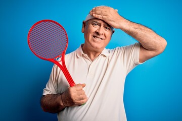 Middle age hoary sportsman playing tennis using racket over isolated blue background stressed with hand on head, shocked with shame and surprise face, angry and frustrated. Fear and upset for mistake.