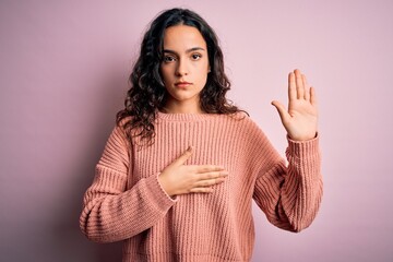 Young beautiful woman with curly hair wearing casual sweater over isolated pink background Swearing...