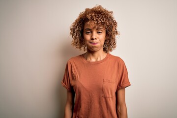Beautiful african american woman with curly hair wearing casual t-shirt over white background puffing cheeks with funny face. Mouth inflated with air, crazy expression.