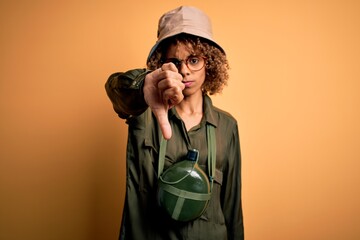 Young african american tourist woman on vacation wearing explorer hat and water canteen looking...