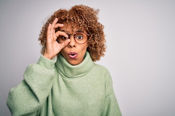 Fototapeta na wymiar Young beautiful african american woman wearing turtleneck sweater and glasses doing ok gesture shocked with surprised face, eye looking through fingers. Unbelieving expression.
