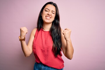 Young brunette woman wearing casual summer shirt over pink isolated background very happy and excited doing winner gesture with arms raised, smiling and screaming for success. Celebration concept.