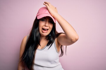 Young brunette woman wearing casual sport cap over pink background surprised with hand on head for mistake, remember error. Forgot, bad memory concept.