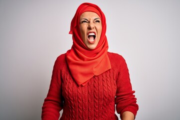 Middle age brunette woman wearing muslim traditional hijab over isolated white background angry and mad screaming frustrated and furious, shouting with anger. Rage and aggressive concept.