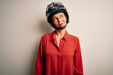 Middle age motorcyclist woman wearing motorcycle helmet over isolated white background smiling looking to the side and staring away thinking.