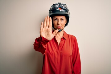 Middle age motorcyclist woman wearing motorcycle helmet over isolated white background doing stop sing with palm of the hand. Warning expression with negative and serious gesture on the face.