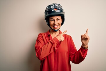 Middle age motorcyclist woman wearing motorcycle helmet over isolated white background smiling and looking at the camera pointing with two hands and fingers to the side.
