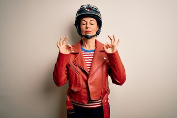 Middle age motorcyclist woman wearing motorcycle helmet and jacket over white background relax and smiling with eyes closed doing meditation gesture with fingers. Yoga concept.