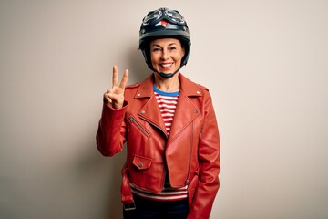 Middle age motorcyclist woman wearing motorcycle helmet and jacket over white background showing and pointing up with fingers number two while smiling confident and happy.