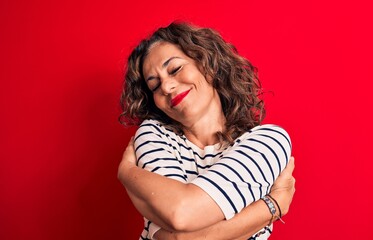 Middle age beautiful brunette woman wearing striped t-shirt standing over red background hugging...