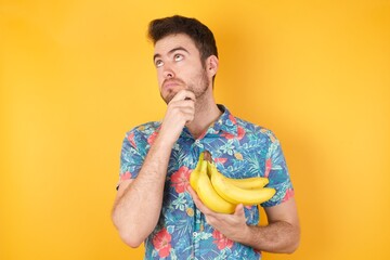 Portrait of thoughtful  man keeps hand under chin, looks away trying to remember something or listens something with interest, dressed casually, poses indoors. Youth concept.