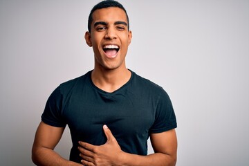 Young handsome african american man wearing casual t-shirt standing over white background smiling and laughing hard out loud because funny crazy joke with hands on body.