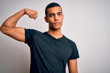 Young handsome african american man wearing casual t-shirt standing over white background Strong person showing arm muscle, confident and proud of power