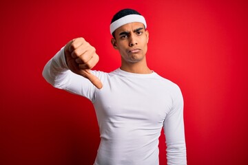 Young handsome african american sportsman wearing sportswear over red background looking unhappy and angry showing rejection and negative with thumbs down gesture. Bad expression.