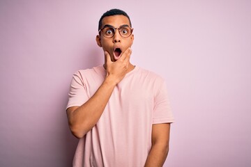 Handsome african american man wearing casual t-shirt and glasses over pink background Looking fascinated with disbelief, surprise and amazed expression with hands on chin
