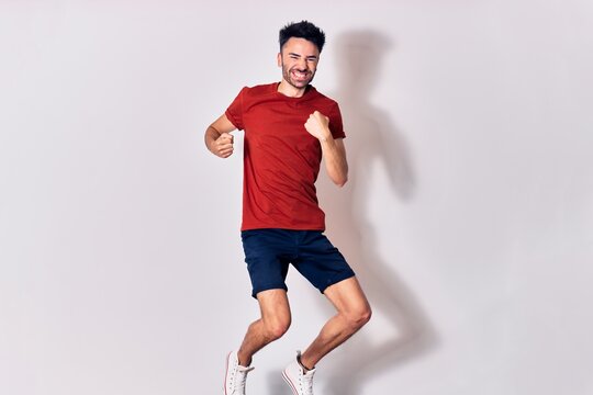 Young handsome man wearing casual clothes smiling happy. Jumping with smile on face doing winner gesture with fists up over isolated white background