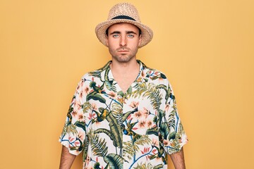 Young handsome man with blue eyes on vacation wearing summer florar shirt and hat with serious expression on face. Simple and natural looking at the camera.
