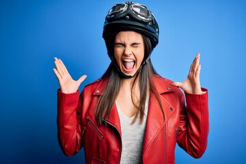 Young beautiful brunette motorcycliste woman wearing motorcycle helmet and jacket celebrating mad...