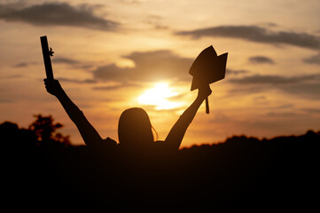 University female graduates Wearing a black robe, wearing a black hat, looking at the sunset