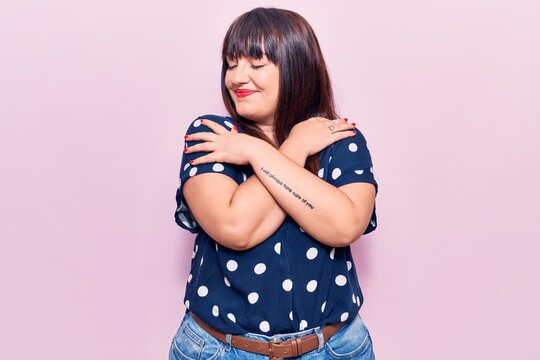 Young plus size woman wearing casual clothes hugging oneself happy and positive, smiling confident. self love and self care