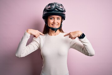Young beautiful motorcyclist woman with blue eyes wearing moto helmet over pink background looking confident with smile on face, pointing oneself with fingers proud and happy.