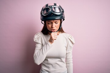 Young beautiful motorcyclist woman with blue eyes wearing moto helmet over pink background feeling unwell and coughing as symptom for cold or bronchitis. Health care concept.
