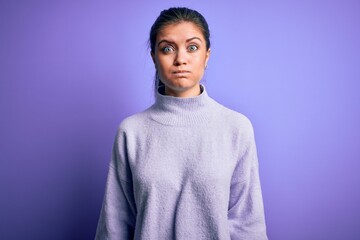 Obraz premium Young beautiful woman with blue eyes wearing casual turtleneck sweater over pink background puffing cheeks with funny face. Mouth inflated with air, crazy expression.