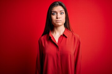 Fototapeta premium Young beautiful woman with blue eyes wearing casual shirt standing over red background puffing cheeks with funny face. Mouth inflated with air, crazy expression.