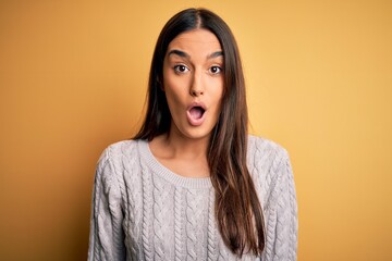 Young beautiful brunette woman wearing white casual sweater over yellow background afraid and shocked with surprise expression, fear and excited face.