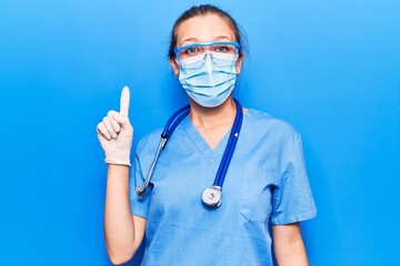Young blonde woman wearing doctor uniform and coronavirus protection holding help reminder smiling with an idea or question pointing finger up with happy face, number one