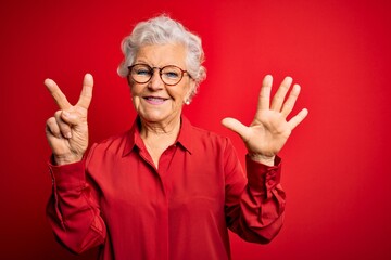 Senior beautiful grey-haired woman wearing casual shirt and glasses over red background showing and...