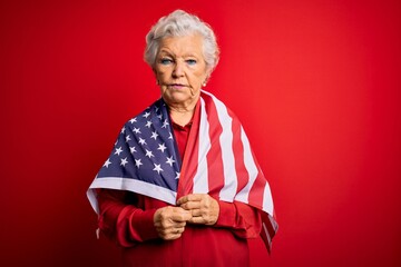 Senior beautiful grey-haired patriotic woman wearing united states flag over red background with a confident expression on smart face thinking serious
