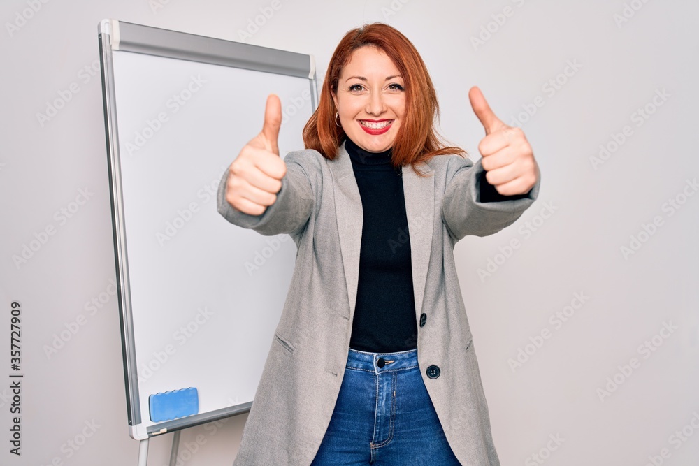 Sticker Young beautiful redhead businesswoman doing business presentation using magnetic board approving doing positive gesture with hand, thumbs up smiling and happy for success. Winner gesture.