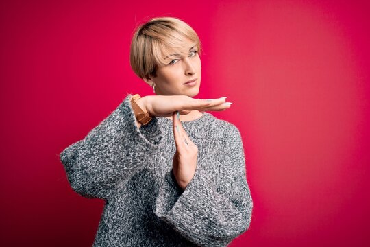 Young blonde woman with modern short hair wearing casual sweater over pink background Doing time out gesture with hands, frustrated and serious face