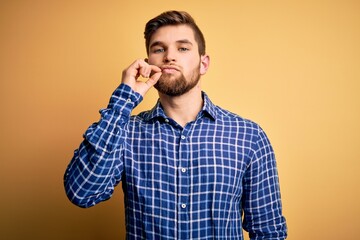 Young blond businessman with beard and blue eyes wearing shirt over yellow background mouth and...