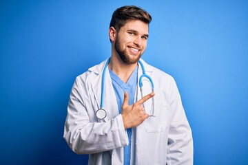 Young blond doctor man with beard and blue eyes wearing white coat and stethoscope cheerful with a smile of face pointing with hand and finger up to the side with happy and natural expression on face
