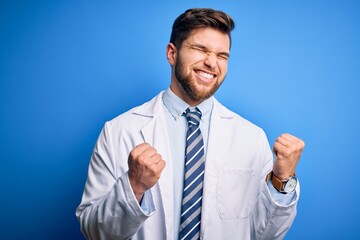 Young blond therapist man with beard and blue eyes wearing coat and tie over background excited for success with arms raised and eyes closed celebrating victory smiling. Winner concept.
