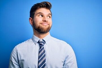 Young blond businessman with beard and blue eyes wearing elegant shirt and tie standing smiling looking to the side and staring away thinking.