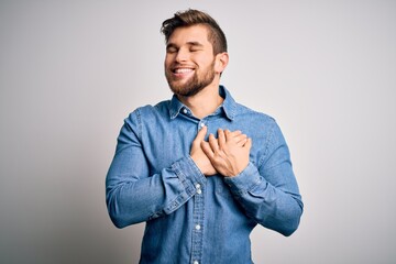 Young handsome blond man with beard and blue eyes wearing casual denim shirt smiling with hands on chest with closed eyes and grateful gesture on face. Health concept.