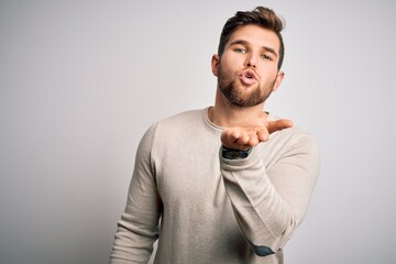 Obraz premium Young handsome blond man with beard and blue eyes wearing casual sweater looking at the camera blowing a kiss with hand on air being lovely and sexy. Love expression.