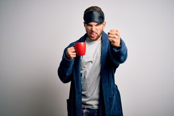 Young blond man with beard and blue eyes wearing pajama drinking cup of coffee annoyed and frustrated shouting with anger, crazy and yelling with raised hand, anger concept