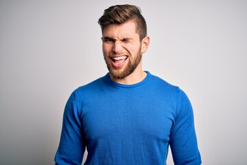 Young handsome blond man with beard and blue eyes wearing casual sweater winking looking at the camera with sexy expression, cheerful and happy face.